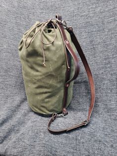 "This is a military style, open top duffel bag, made out of waxed canvas, with 10 ounce latigo leather straps. Each bag is 10\" wide, 18\" tall and holds 24.5 L. Each bag has a single leather strap running up the back, with an attached handle and a removable shoulder strap that connects to D rings on the top and bottom of the bag. The Bag cinches closed with a length of paracord which can be tied, or pressure fit closed with the included leather cincher. These bags are made out of fairly heavy w Waxed Canvas Duffle Bag With Leather Trim For Outdoor, Canvas Duffle Bag With Waxed Finish For Outdoor Activities, Waxed Canvas Duffle Bag For Outdoor Activities, Everyday Canvas Duffle Bag With Waxed Finish, Rugged Waxed Finish Duffle Bag For Everyday Use, Leather Duffle Bag With Waxed Finish For Outdoor, Waxed Finish Satchel Duffle Bag For Everyday Use, Outdoor Waxed Canvas Weekender Bag With Waxed Finish, Canvas Duffle Bag With Adjustable Strap For Outdoor