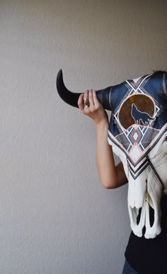 a woman holding up a cow's skull with an animal mask on her head