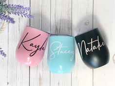 three wine glasses with names on them sitting next to a purple and blue flower vase