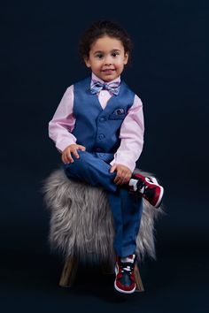 a little boy sitting on top of a chair wearing a blue suit and bow tie