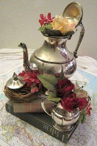 a silver tea pot sitting on top of a pile of books with flowers in it