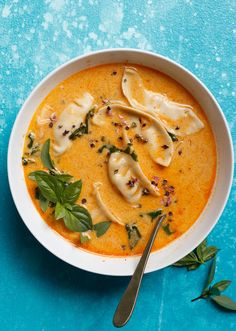 a white bowl filled with soup on top of a blue table next to a spoon