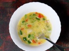 a white bowl filled with soup sitting on top of a wooden table next to a spoon