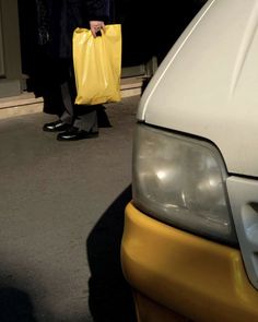 a man holding a yellow shopping bag next to a white car