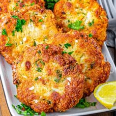 three crab cakes on a white plate with lemon wedges and garnished parsley