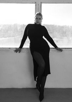 a woman leaning against a wall with her legs on the window sill and looking at the camera