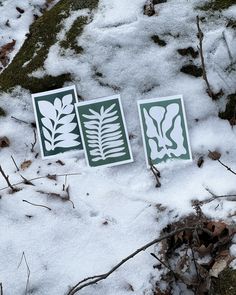 three green and white leaf stencils laying in the snow on top of some grass