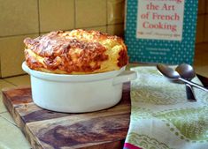 a casserole sitting on top of a wooden cutting board next to a book