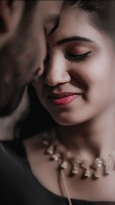 a man kissing a woman's forehead while she is wearing a necklace and earrings