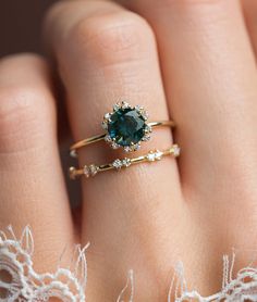 a woman's hand holding a ring with a green stone in the middle and white lace around it