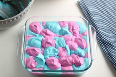 a blue and pink cake in a glass dish on a table next to a bowl