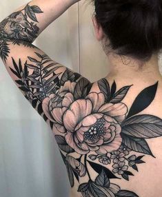 the back of a woman's shoulder with flowers and leaves tattooed on her arm