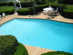 an empty swimming pool surrounded by hedges and lawn furniture