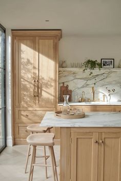 a kitchen with marble counter tops and wooden cabinets, along with two stools in front of the island