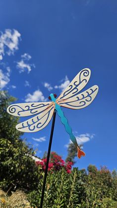 a dragon shaped wind spinner sitting on top of a wooden post in front of some bushes