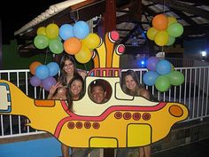 some people are posing in front of a yellow submarine shaped boat with balloons on it