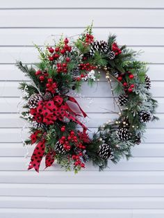 a christmas wreath hanging on the side of a white building with pine cones and red berries