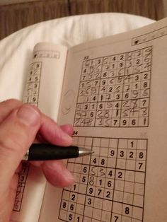 a person is holding a pen and looking at a sud puzzle book with numbers on it