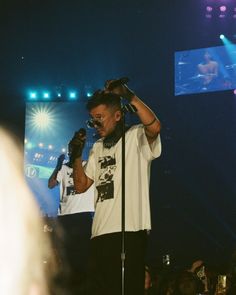 a man standing on top of a stage holding a microphone to his ear and singing