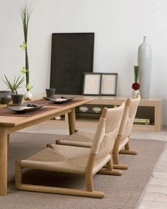 a wooden table with chairs and vases on it next to a rug in front of a white wall