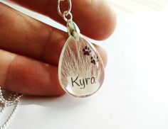 a person holding a necklace with a dog's paw and name in the tear