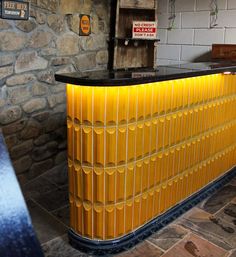 a yellow and black counter top sitting in front of a stone wall with signs on it