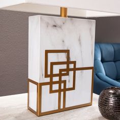 a white marble block with gold accents on a table next to a blue chair and lamp