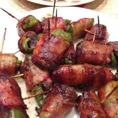 several skewered meats and peppers on a white plate with toothpicks