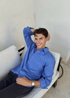 a young man sitting on top of a white chair next to a wall and smiling