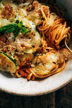 a white bowl filled with pasta and meat covered in sauce, parmesan cheese and herbs