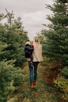 a mother and her child walking through a christmas tree farm in the woods with their back to the camera