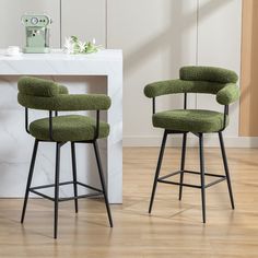 two green upholstered barstools sit in front of a white marble counter