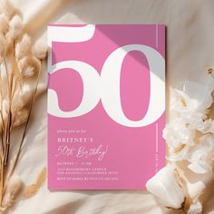 a pink 50th birthday party card with white numbers and flowers next to it on a bed