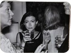 black and white photograph of three women holding glasses in their hands while talking to each other