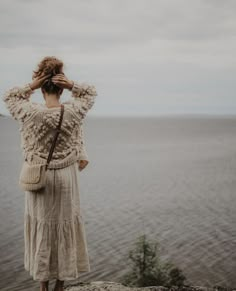 a woman standing on top of a cliff next to the ocean looking at the water