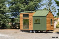 a small green and brown house sitting on the side of a road next to trees