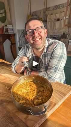 a man sitting at a table with a pan of food in front of him on top of a cutting board