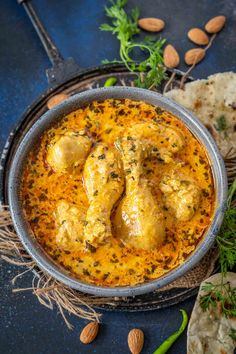 chicken curry in a bowl with almonds and herbs on the side, along with pita bread