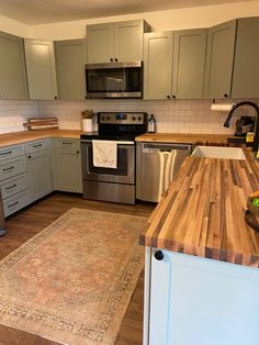 a kitchen with stainless steel appliances and wooden counter tops, along with a rug on the floor