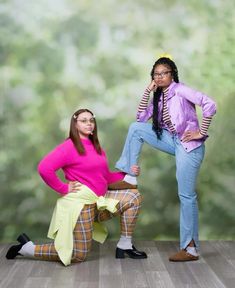 two young women posing for a photo in front of a green background, one wearing a pink shirt and the other yellow skirt