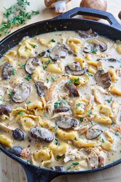 a skillet filled with pasta and mushrooms on top of a wooden table next to some parsley