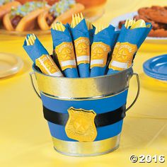 a bucket filled with blue and yellow napkins sitting on top of a table next to cookies