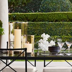 a table with candles and vases on it in front of a wall full of hedges