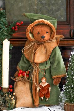 a teddy bear dressed in a green outfit next to a lit candle and christmas tree