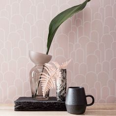 a vase with a plant in it sitting on a table next to a mug and wallpaper