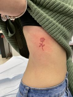 a small rose tattoo on the back of a woman's rib - up stomach