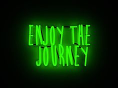 the words enjoy the journey are lit up in bright green neon letters on a black background