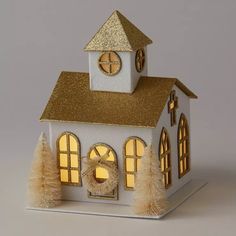 a small white house with a clock on the front and windows, lit up at night