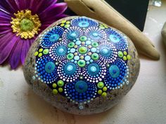 a painted rock next to a purple flower