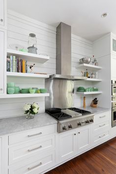 a stove top oven sitting inside of a kitchen next to white cupboards and shelves